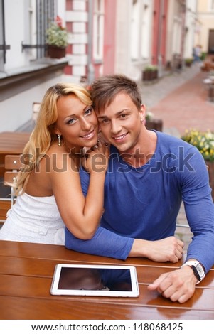 Stylish happy young couple with tablet pc behind table in a summer cafe