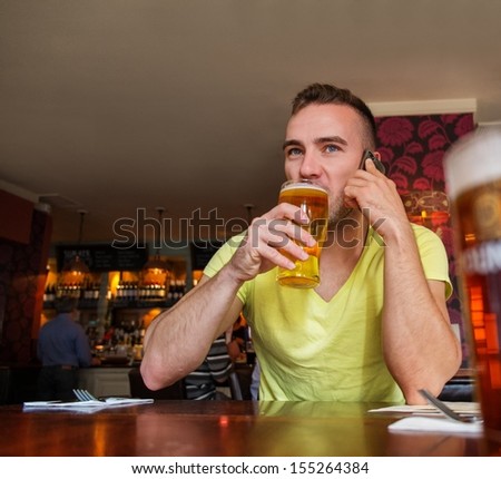 Handsome young man with mobile phone and beer in a pub