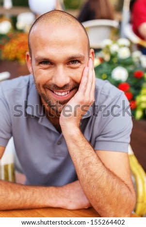 Positive middle-aged man alone behind table in summer cafe