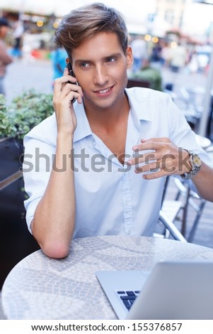 Handsome young man with laptop and mobile phone calling in a summer cafe