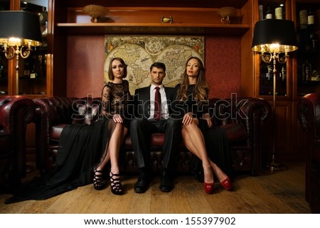 Handsome Brunette Wearing Suit Sitting On Sofa With Two Beautiful Women
