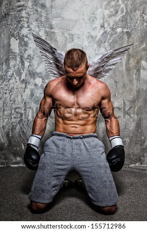 Young boxer with angel wings behind his back standing on his knee