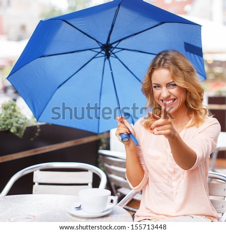 Beautiful girl with blue umbrella sitting in summer cafe