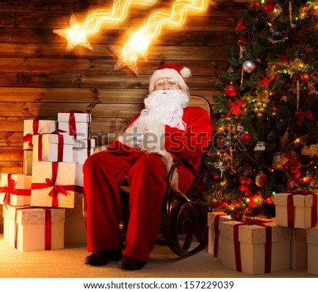 Santa Claus sitting on rocking chair in wooden home interior with gift boxes around him and two falling stars