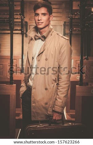 Handsome young man with suitcase in coat inside vintage train coach