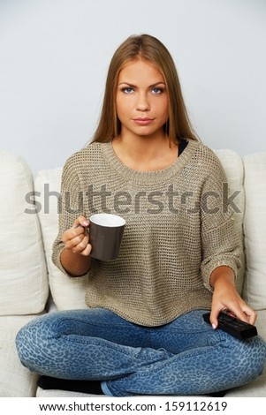 Young beautiful woman on a sofa with remote control and mug
