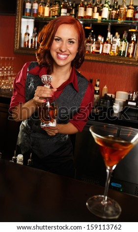 Beautiful redhead barmaid with bottle behind bar counter
