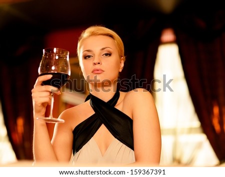 Beautiful blond woman in evening with glass of red wine