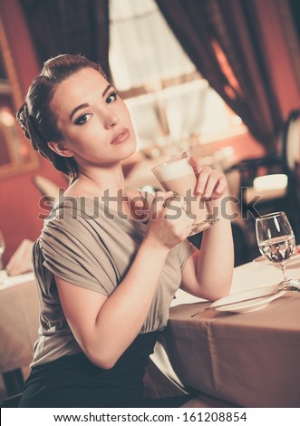 Beautiful young girl with cup of coffee alone in a restaurant