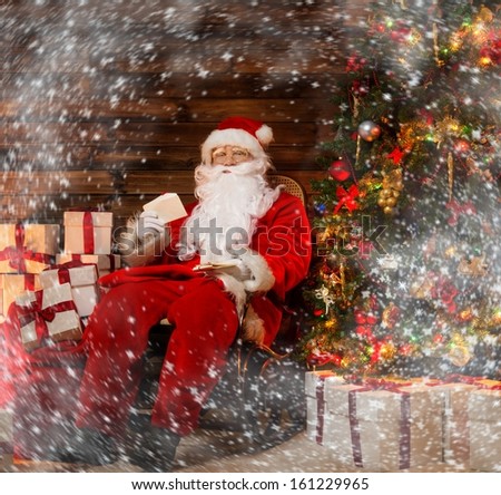 Santa Claus sitting on rocking chair in wooden home interior with letters in hands