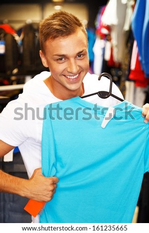 Handsome young man choosing t-shirt in a sport outlet