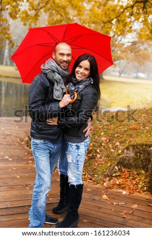 Happy middle-aged couple with umbrella outdoors on beautiful rainy autumn day