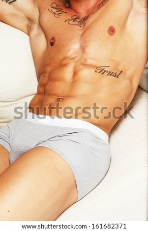 Man with beautiful muscular tattooed torso in underwear lying on sofa