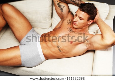 Man With Beautiful Muscular Tattooed Torso In Underwear Lying On Sofa