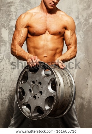 Handsome sporty man with muscular body holding alloy wheel