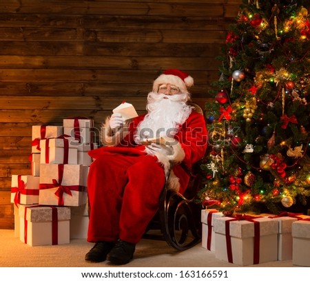 Santa Claus sitting on rocking chair in wooden home interior with letters in hands