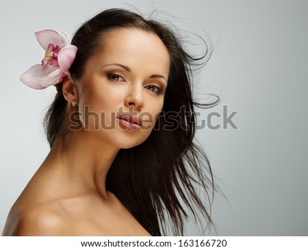 Young beautiful brunette woman with orchid flower in her waving hair