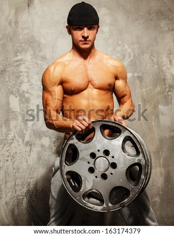 Handsome sporty man with muscular body holding alloy wheel