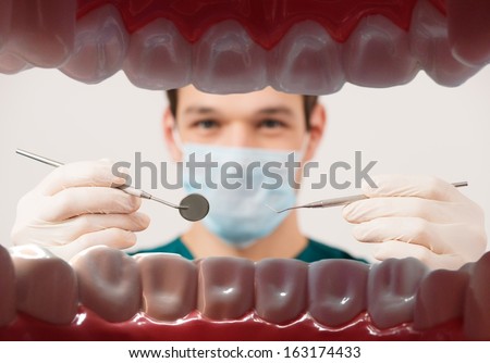 View at young male dentist holding dental tools from patient mouth