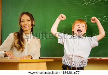 Little happy redhead boy answering near blackboard in school