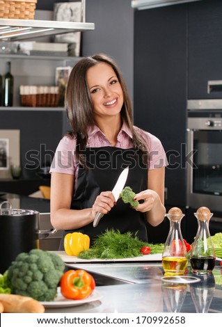 Happy young woman in apron on modern kitchen cutting vegetables