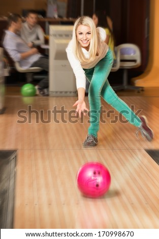 Young smiling blond woman throwing ball in a bowling club