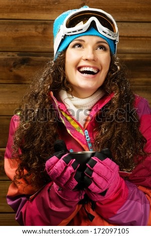Happy woman in ski wear with cup of a hot drink against wooden wall