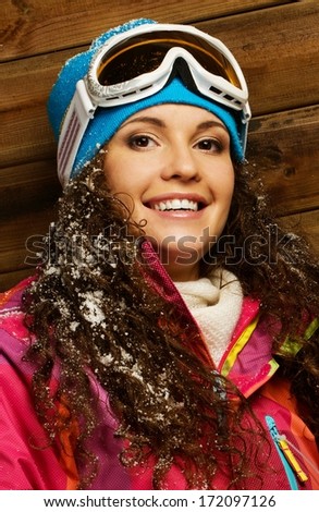 Smiling woman in ski jacket and ski mask against wooden house wall