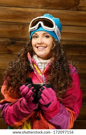Happy woman in ski wear with cup of a hot drink against wooden wall