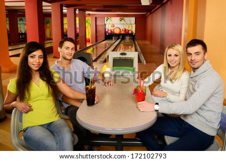 Group of four young smiling people chatting behind table in bowling club