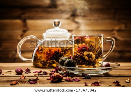 Teapot And Glass Cup With Blooming Tea Flower Inside Against Wooden Background