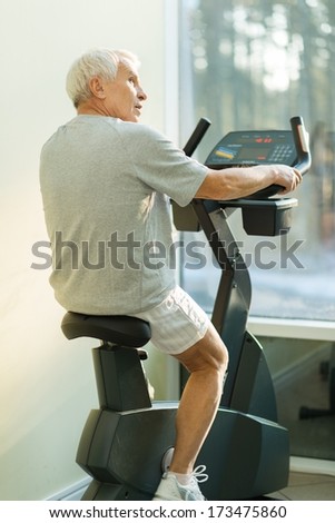 Senior man doing exercise on a bike in a fitness club