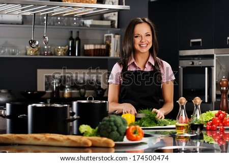 Cheerful Young Woman In Apron On Modern Kitchen Cutting Vegetables