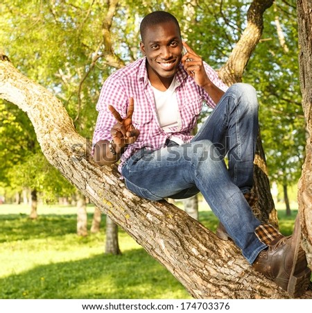 Young smiling african american sitting on a tree in park with mobile phone