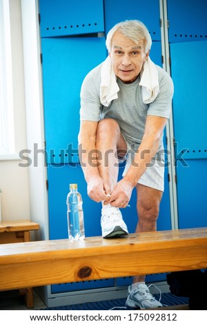 Senior man tying up sneakers in fitness club locker room