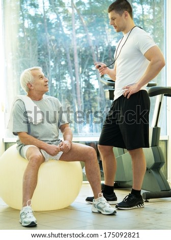 Personal trainer explains to a senior man how to do exercise on a fitness ball