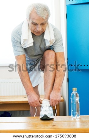 Senior man tying up sneakers in fitness club locker room