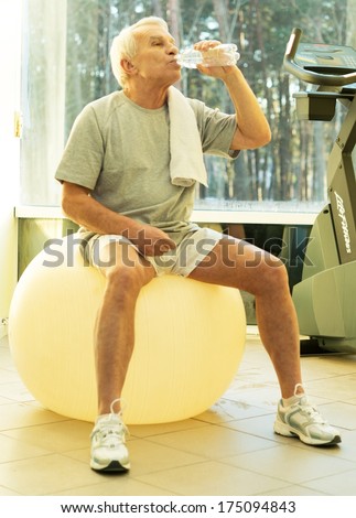 Tired senior man with towel and bottle of water on exercise fitness ball