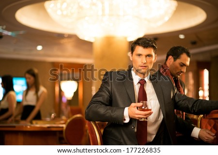 Two Young Men In Suits Behind Gambling Table In A Casino