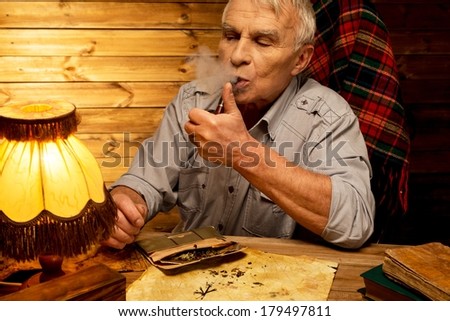 Senior man with smoking pipe in homely wooden interior