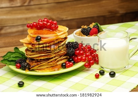 Healthy breakfast with pancakes, fresh berries and milk on tablecloth in rural interior