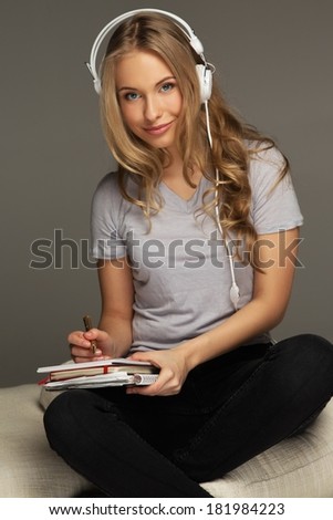 Positive young woman student with notebook listens to music