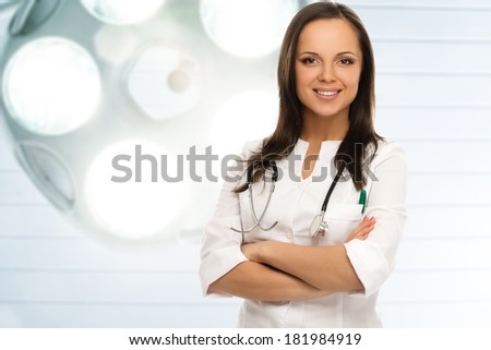 Young positive brunette doctor against lamp in surgery room