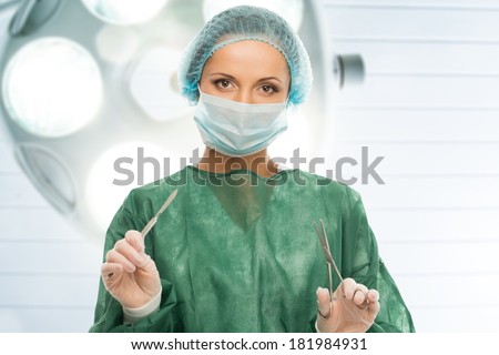 Young woman doctor with scalpel and scissors in surgery room interior