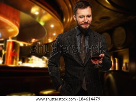 Handsome well-dressed man in jacket with glass of beverage in restaurant interior