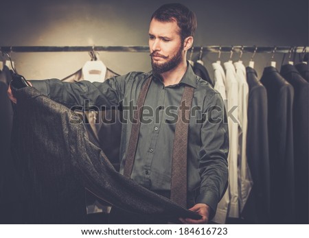 Handsome man with beard choosing jacket in a shop