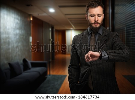 Handsome well-dressed man with beard looking at his wrist watch in a hallway