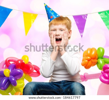 Funny little redhead boy among birthday balloons