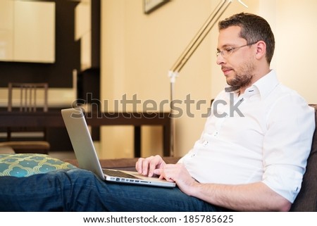 Young man with gray hair with laptop on sofa in home interior