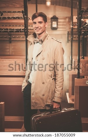 Handsome young man with suitcase in coat inside vintage train coach